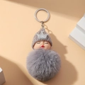 Detail eines schlafenden Puppen-Plüsch-Schlüsselanhängers mit grauem Pelzball und Krone - Grau