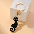 Eleganter schwarzer Katzen-Schlüsselanhänger mit Goldring und weißer Perle auf Stein - Schwarz