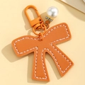 Detailed view of orange PU leather bow keychain with pearl charm and white stitching - Orange