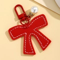 Detail of red PU leather bow keychain with white stitching and white pearl pendant charm - Red
