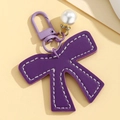 Detail of purple leather bow keychain with contrast stitching and pearl pendant accessory - Purple