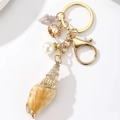 Dettaglio del portachiavi a tema marino con conchiglia naturale e grande perla bianca - Stile 4