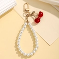 Close-up of pearl chain keychain with red cherry charm and golden metal leaf detail - Red