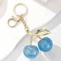 Detail von blauem Kirsch-Schlüsselanhänger mit Goldblättern auf weißem Podest - Glitzer Blau