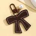 Detail of a brown leather bow keychain with white stitching and a faux pearl accent - Dark Coffee