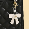 Détail d'un charme nœud en cuir blanc avec perle sur un sac à main noir matelassé - Blanc