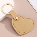 Détail d'un porte-clés coeur en similicuir marron clair avec couture et anneau doré - Kaki
