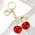 Detailed view of glossy red cherry keychain with polished gold leaves on white stand - Mirror Red