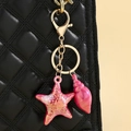 Nahaufnahme von rosa Seestern- und Muschelanhängern an einer schwarzen Stepptasche - Fuchsia