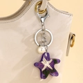 Dettaglio di un portachiavi a stella marina viola con perla su una borsa beige chic - Viola