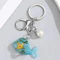 Llavero de ballena de resina azul océano con estrella de mar y perla en fondo gris - Azul claro