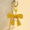 Détail d'un nœud porte-clés jaune en cuir PU avec perle centrale et strass brillants - Jaune