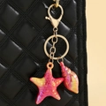 Detail of colorful resin starfish and conch keychain on a black quilted handbag - Red