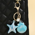 Close-up of colorful seashell and starfish keychain pendant on a black quilted bag - Blue