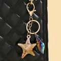 Macro detail of iridescent starfish and conch pendant charm on black quilted bag - Khaki