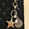 Detail of colorful ocean shell and starfish keychain charm on black quilted leather bag - Khaki