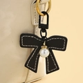 Detail eines schwarzen Leder-Schleifenanhängers mit weißen Nähten und Perle an einer Tasche - Schwarz