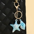 Detail of colorful seashell and starfish keychain hanging on a black quilted bag - Blue