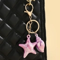 Macro view of colorful gradient starfish and conch keychain on a quilted black leather bag - Purple