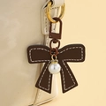 Détail d'un pendentif noeud en cuir marron avec surpiqûres et perle élégante - Café Foncé