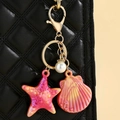 Detail of seashell and starfish keychain with gold hardware on a black leather bag - Red