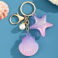 Detalle de colgantes de estrella de mar y concha en acrílico con llavero dorado premium - Rosa Púrpura