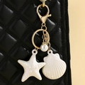 Detail of starfish and shell charms with pearls hanging on a black quilted leather bag - White