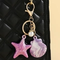 Detail of starfish and shell charms with iridescent finish on a black leather bag - Purple