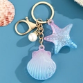 Detalle de llavero de concha de acrílico con anillo dorado y colgante de estrella - Azul Pálido
