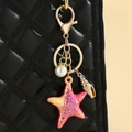 Pink and orange resin starfish keychain with pearl detail on a black quilted bag - Red