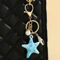 Primer plano de llavero de estrella de mar con perla en bolso acolchado negro - Azul