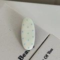Détail d'une pince à cheveux ovale crème à pois bleu clair sur surface texturée - Clip Ovale Blanc Crème Points Bleus