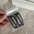Macro shot of 4-piece matte black water-drop BB hair clips in transparent packaging - Black Triangle Style