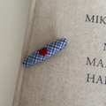 Détail d'une pince à cheveux à carreaux bleus avec un cœur rouge 3D sur fond texturé - Ovale Bleu Cœur Rouge
