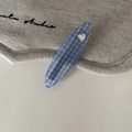 Detail der blau-weiß karierten Haarspange mit Herz-Strassstein auf Leinenstoff-Hintergrund - Ellipse