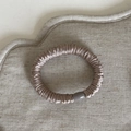 Dettaglio macro dello scrunchie in seta champagne con trama a pieghe e fibbia grigia - modello base / Champagne