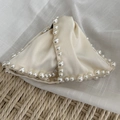 Detail of elegant cream bow hair claw with delicate pearl bead edges and silk texture - White