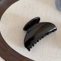 Polished black jelly hair claw clip with minimalist curved design on a dark wood tray - Black