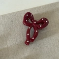 Detail view of a cherry red polka dot bow hair clip on a textured beige background - Bow Claw Clip