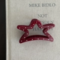 Detail view of a star-shaped burgundy hair claw clip with white polka dots on a book cover - Star Style