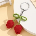 Close-up of handmade knitted red tulip flower bud keychain with green bow on white stand - Red