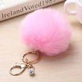 Détail d'un porte-clés en fourrure rose avec boule en strass sur une surface en bois - 8cm / Rose