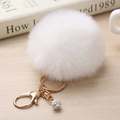 Détail du porte-clés pompon blanc avec anneau doré et perles strass sur table en bois clair - 8cm / Blanc