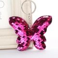 Détail d'un porte-clés papillon à paillettes magenta suspendu à un cadre blanc décoratif - 12x9 / Rouge Rose