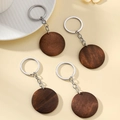 Set of four round dark wood keychains with silver metal rings on a beige background - Coffee