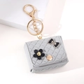 Dettaglio mini ciondolo grigio trapuntato con moschettone dorato e decorazioni floreali - Portachiavi borsa stile trapuntato / Grigio