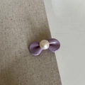 Dettaglio di un fermaglio a fiocco viola con perla bianca su tessuto beige strutturato - Viola