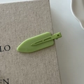 Matte avocado green flat alligator hair clip on a textured beige woven background - Green