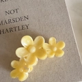 Gros plan d'une pince à cheveux marguerite jaune crème en acétate sur un livre - Pince Jaune à Trois Fleurs
