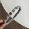 Detail eines schwarz-weiß karierten Haarreifs mit goldenem Hand made Metallemblem - Schwarz-weiß kariert